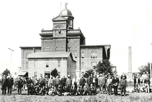 Another Picture of the Buffalo County Courthouse, completed in 1890. The old courthouse donated by the Union Pacific Railroad in the foreground, with the members of the Board of Supervisors.